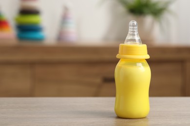 Photo of Feeding bottle with baby formula on wooden table indoors. Space for text