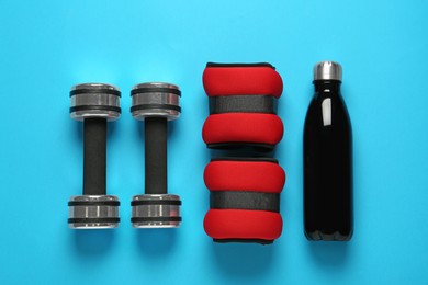 Photo of Red weighting agents, dumbbells and sport bottle on light blue background, flat lay
