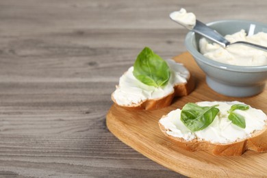 Photo of Delicious sandwiches with cream cheese and basil leaves on wooden table, closeup. Space for text