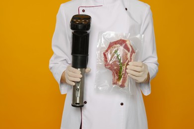 Photo of Chef holding sous vide cooker and meat in vacuum pack on orange background, closeup