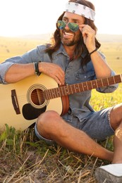 Portrait of happy hippie man with guitar in field