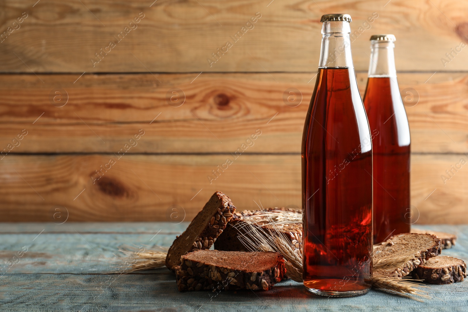 Photo of Bottles of delicious fresh kvass, spikelets and bread on blue wooden table. Space for text