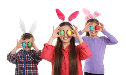 Photo of Cute family in bunny ears headbands with Easter eggs near eyes on white background