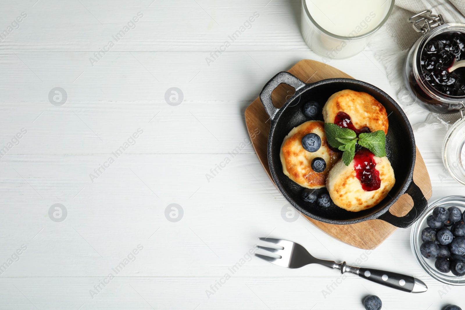 Photo of Delicious cottage cheese pancakes with blueberries, mint and jam on white wooden table, flat lay. Space for text