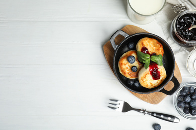 Photo of Delicious cottage cheese pancakes with blueberries, mint and jam on white wooden table, flat lay. Space for text