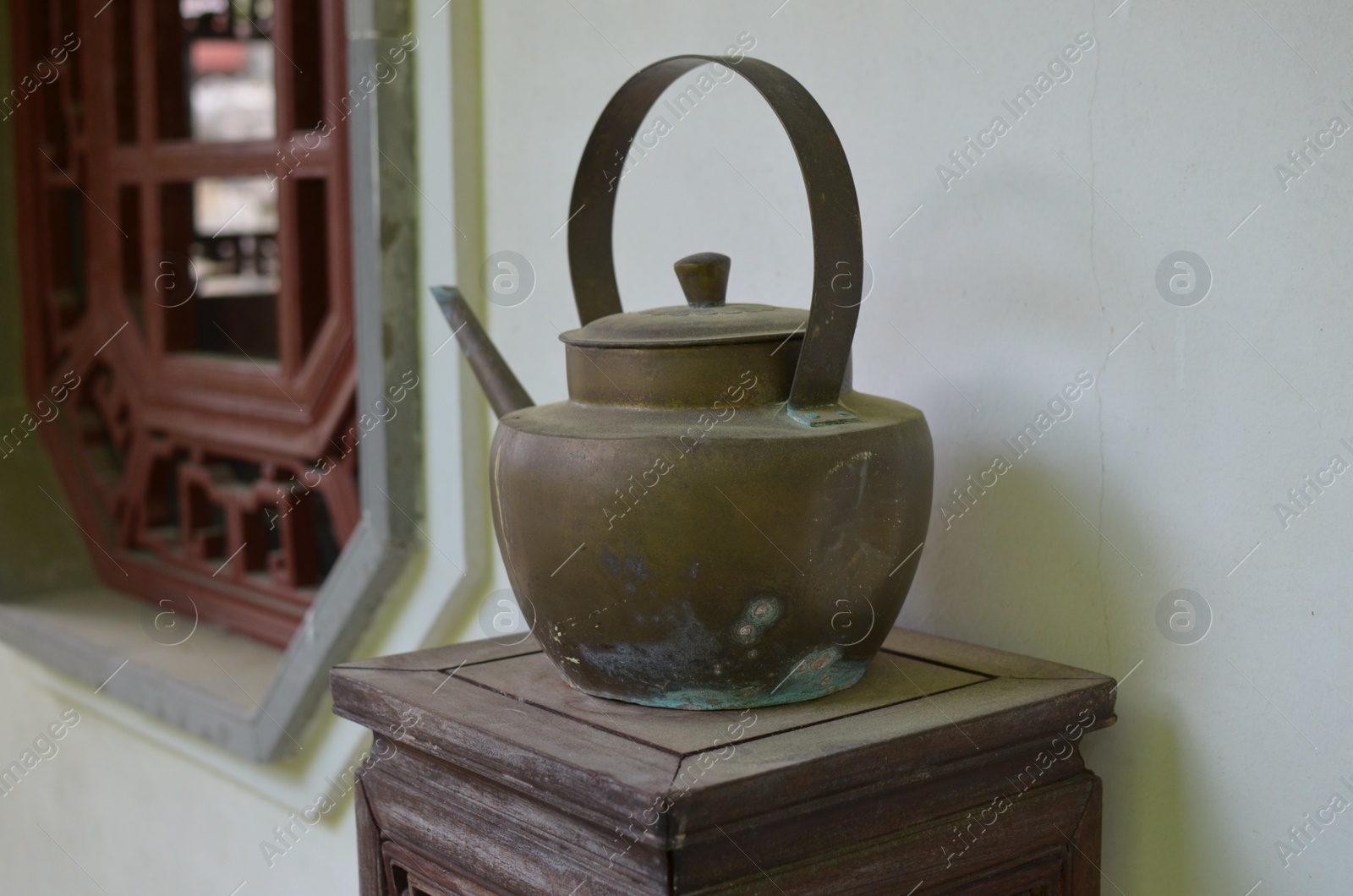 Photo of Old metal kettle on wooden stand in room. Decorative element