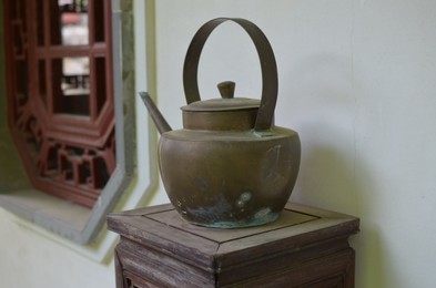 Photo of Old metal kettle on wooden stand in room. Decorative element