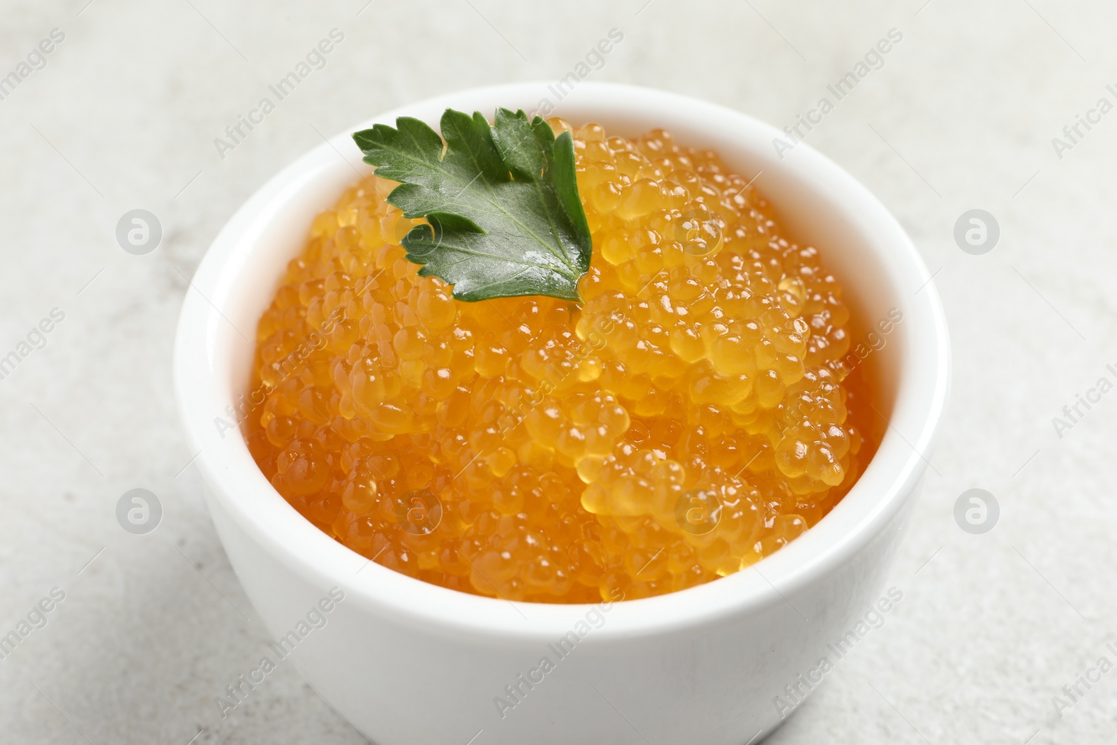 Photo of Fresh pike caviar and parsley in bowl on light grey table, closeup