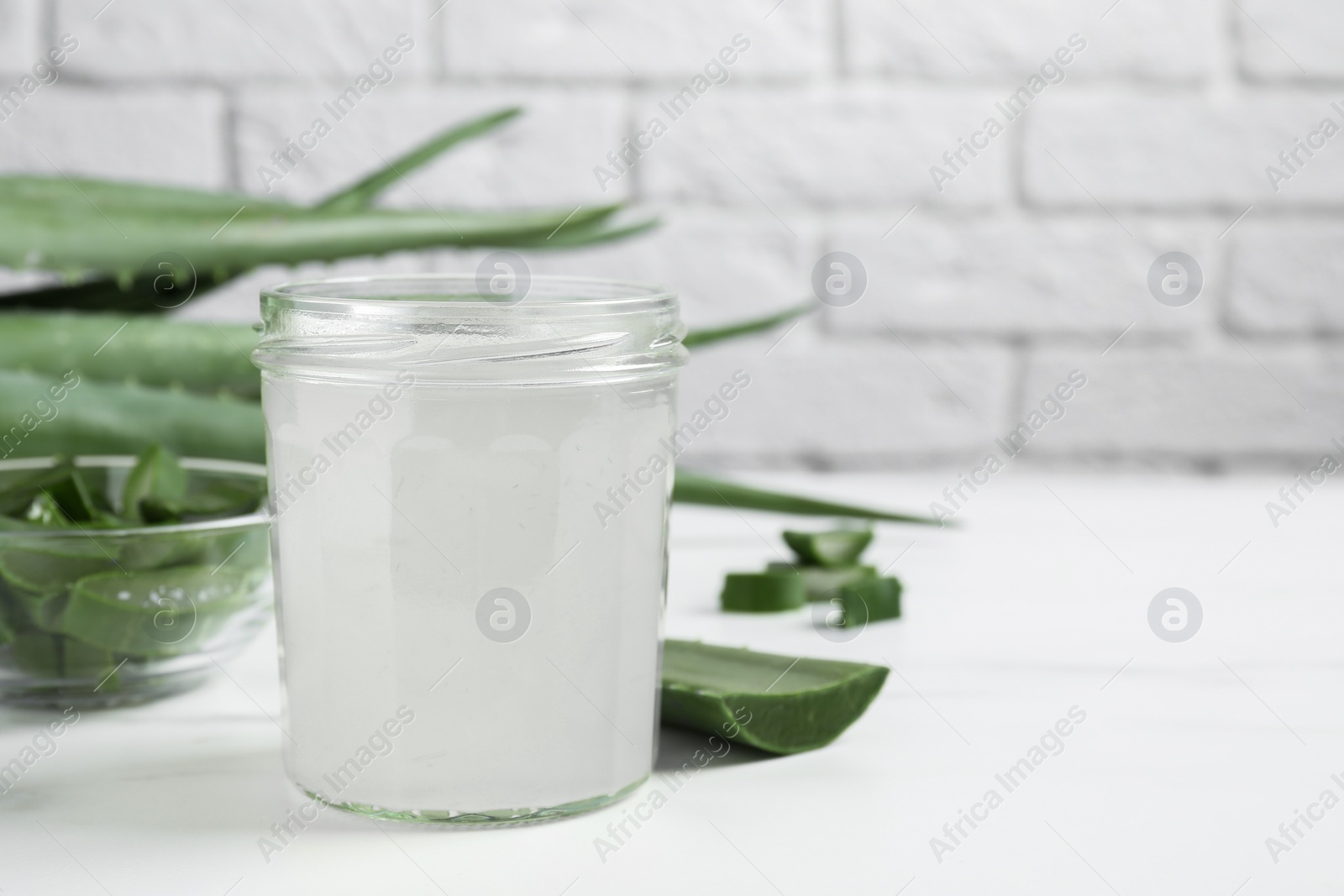 Photo of Fresh aloe juice in jar and leaves on white table, closeup. Space for text