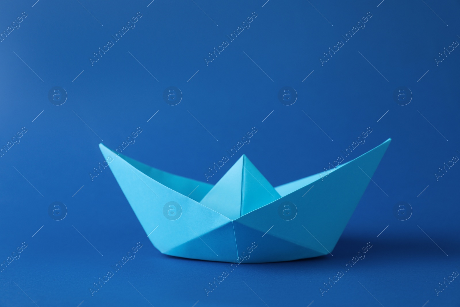 Photo of Handmade paper boat on blue background. Origami art