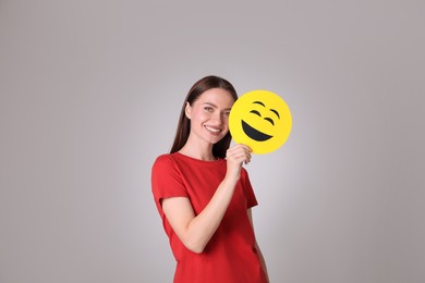 Happy young woman with laughing emoji on grey background