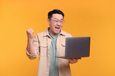 Emotional man with laptop on yellow background