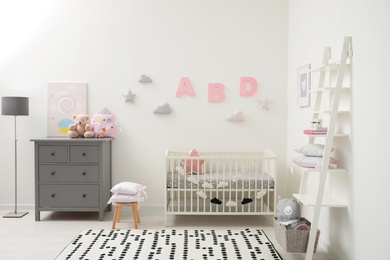 Cute baby room interior with crib and chest of drawers near white wall