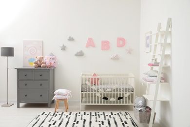 Photo of Cute baby room interior with crib and chest of drawers near white wall