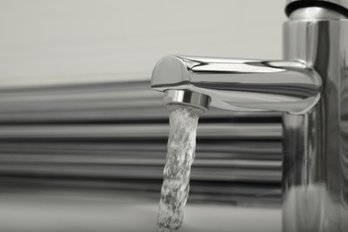 Photo of Water flowing from tap on blurred background, closeup. Space for text