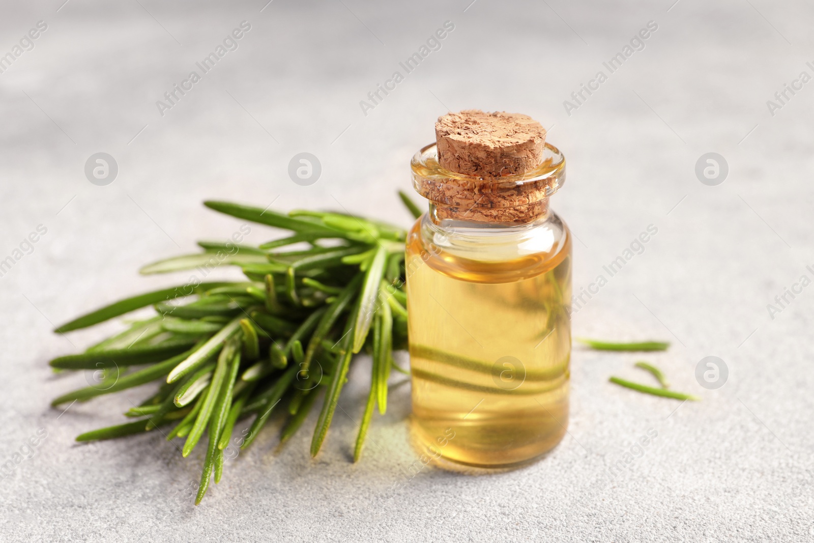 Photo of Bottle with essential oil and fresh rosemary on light textured table, closeup