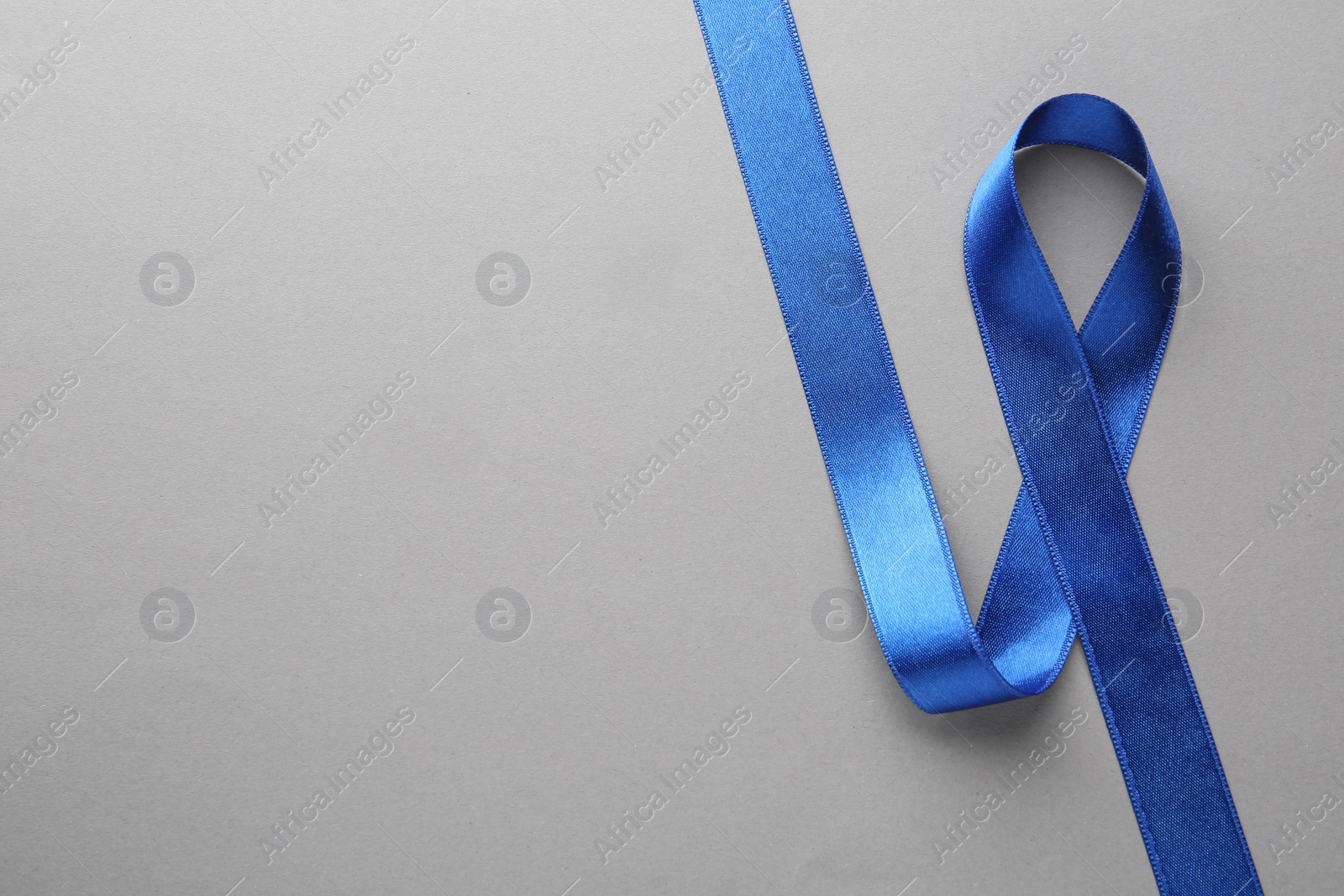 Photo of Blue awareness ribbon on grey background, top view with space for text. Symbol of social and medical issues