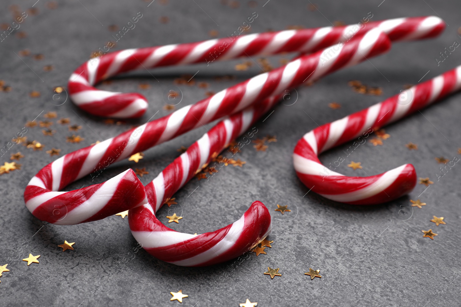 Photo of Many sweet Christmas candy canes and shiny confetti on grey background