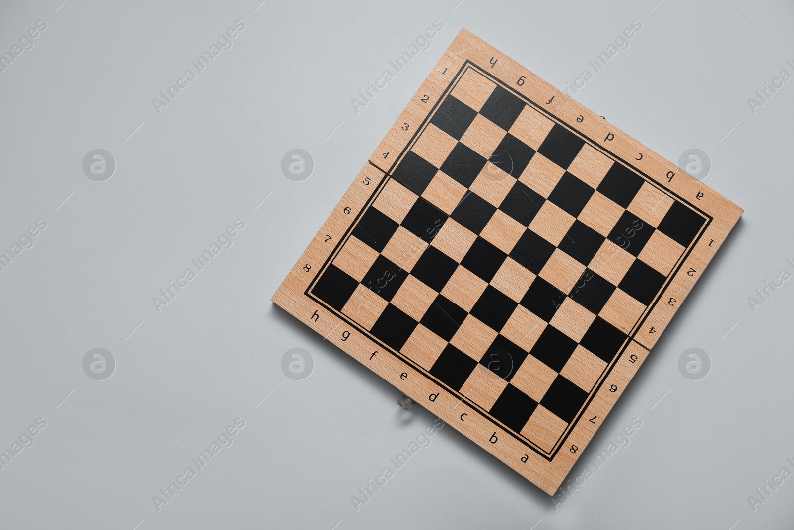 Photo of Empty wooden checkerboard on light grey background, top view. Space for text