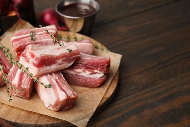 Photo of Cut raw pork ribs with thyme on wooden table. Space for text