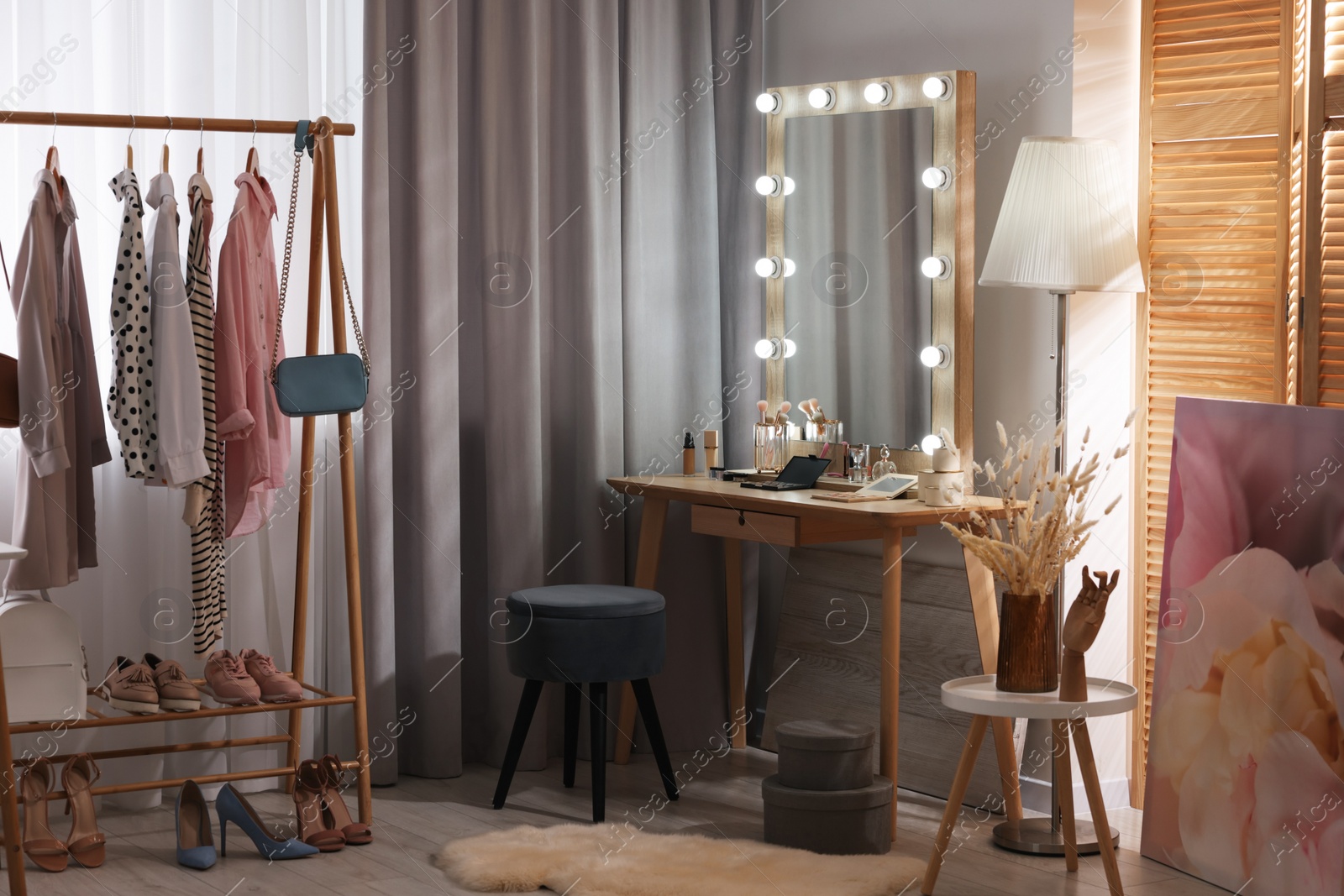 Photo of Makeup room. Stylish dressing table with mirror, chair and clothes rack indoors