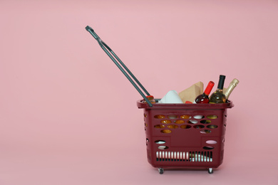 Shopping basket full of different products on pink background. Space for text