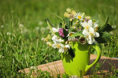 Photo of Green cup with different wildflowers and herbs on wooden board in meadow. Space for text