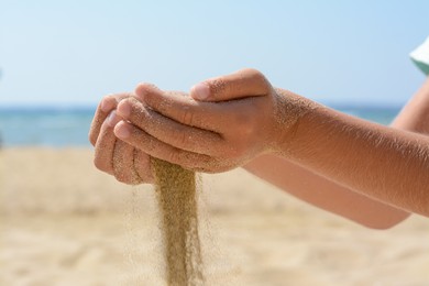 Photo of Child pouring sand from hands on beach near sea, closeup. Fleeting time concept