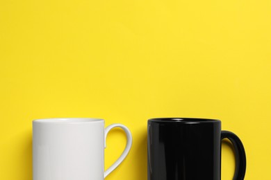 Photo of Black and white ceramic mugs on yellow background, flat lay. Space for text