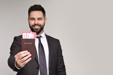 Happy businessman showing passport and tickets on grey background, selective focus. Space for text