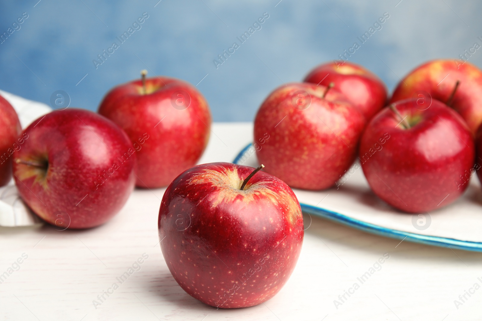 Photo of Ripe juicy red apples on white wooden table against blue background