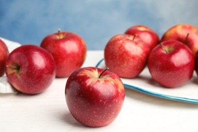 Photo of Ripe juicy red apples on white wooden table against blue background