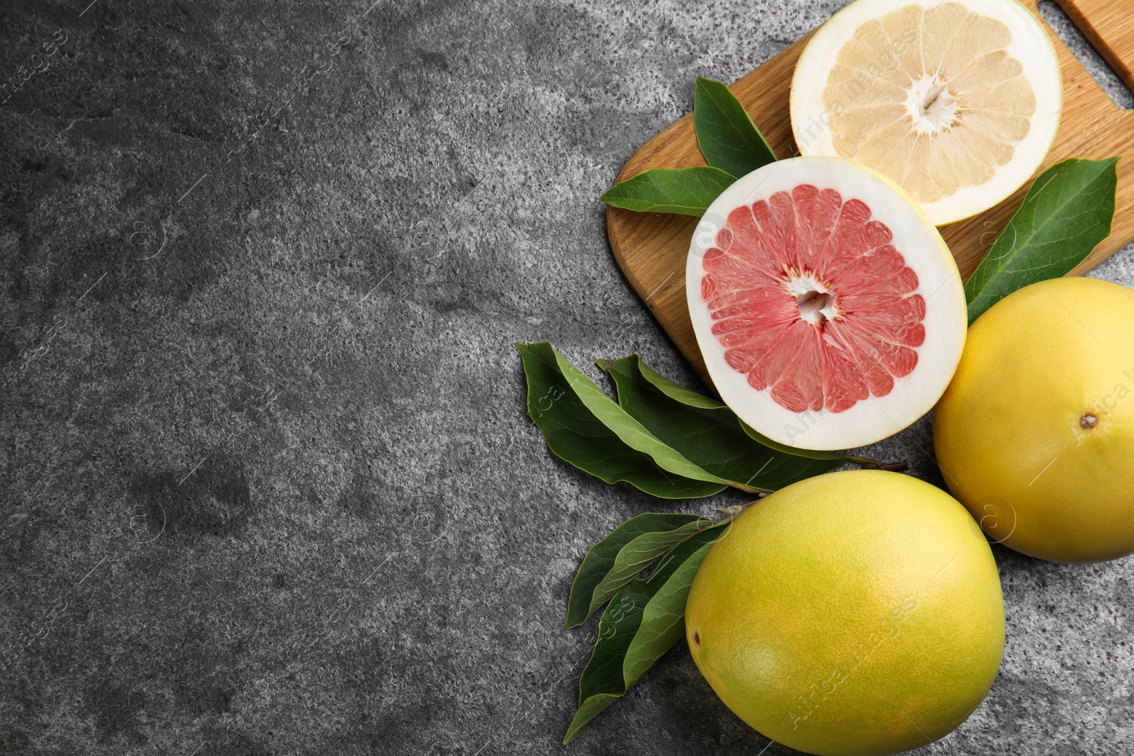 Photo of Fresh cut and whole pomelo fruits with leaves on grey table, flat lay. Space for text