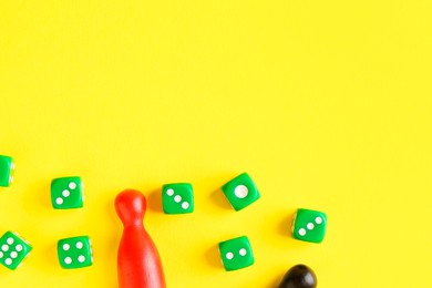 Photo of Many green dices and color game pieces on yellow background, flat lay
