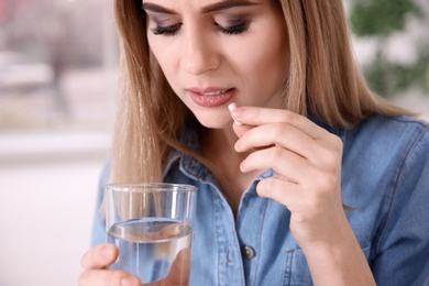 Photo of Young woman taking pill indoors