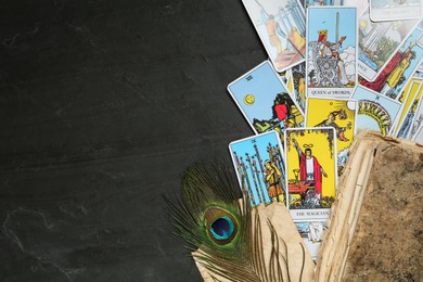 Photo of Tarot cards, old book and peacock feather on black table, flat lay. Space for text