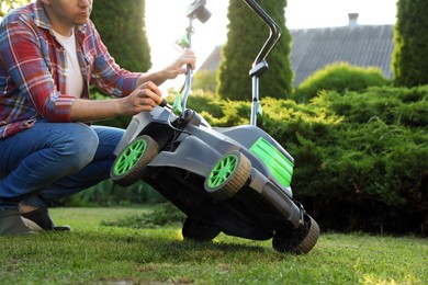 Man with screwdriver fixing lawn mower in garden, closeup