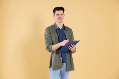 Photo of Handsome young man writing on clipboard against beige background