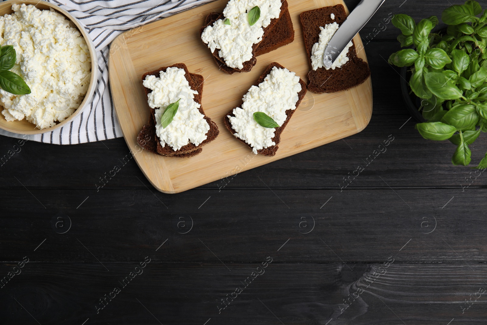 Photo of Bread with cottage cheese and basil on black wooden table, flat lay. Space for text