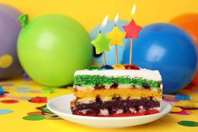 Piece of birthday cake with candles on yellow background