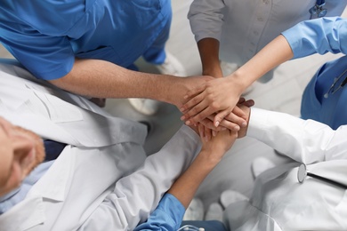 Photo of Young medical doctors putting hands together indoors, top view. Unity concept