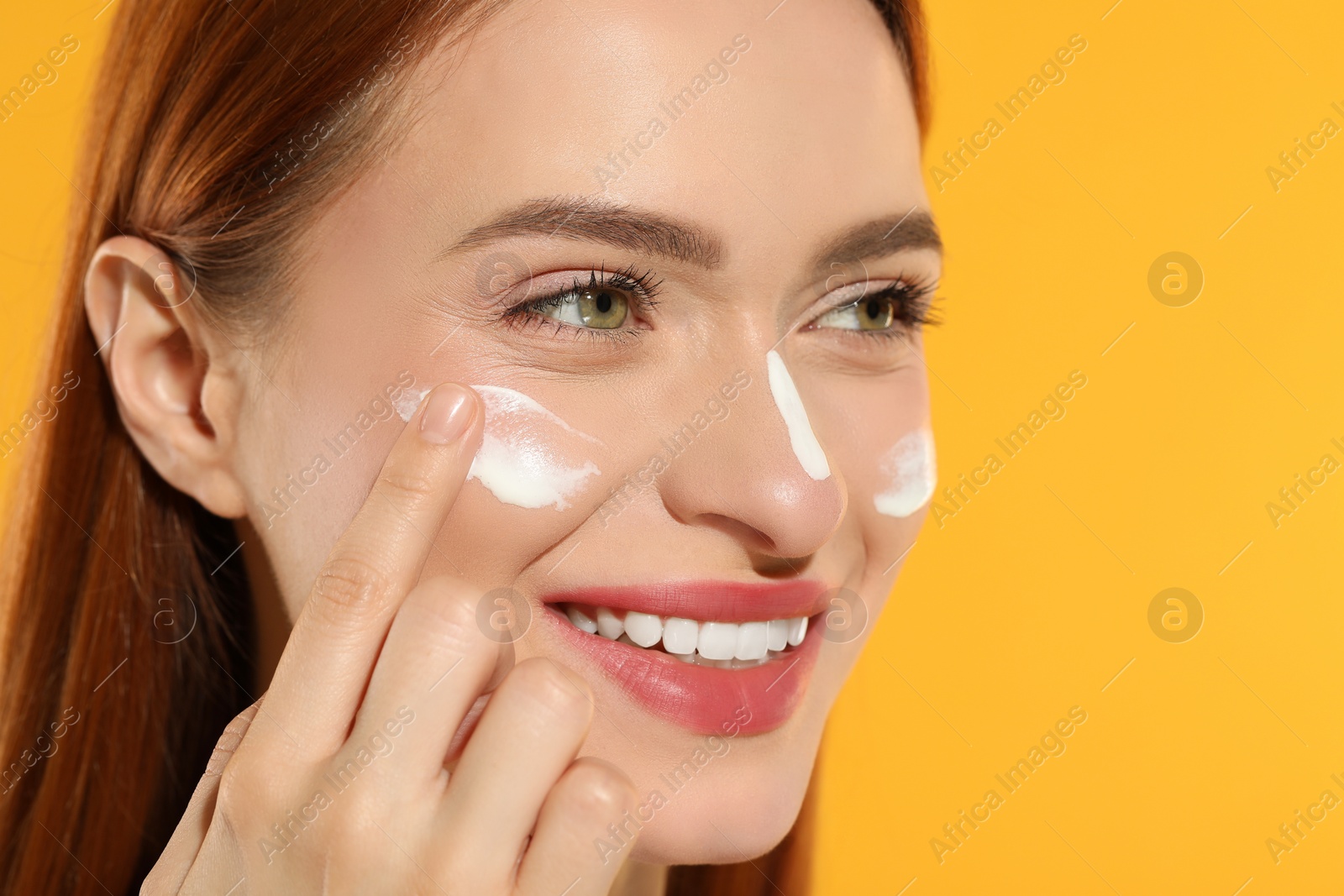 Photo of Beautiful young woman with sun protection cream on her face against orange background, closeup. Space for text