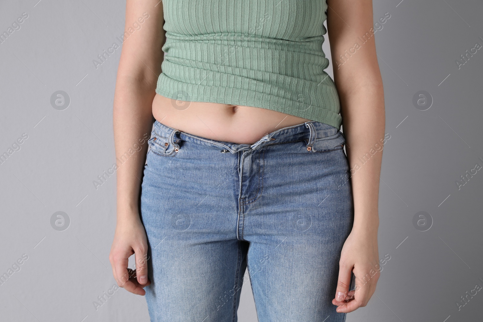 Photo of Woman wearing tight clothes on light grey background, closeup. Overweight problem