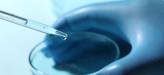 Photo of Doctor dripping liquid from pipette into petri dish on blurred background, closeup. Laboratory analysis