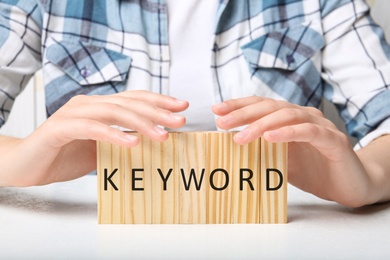 Photo of Woman demonstrating blocks with word KEYWORD at white table, closeup
