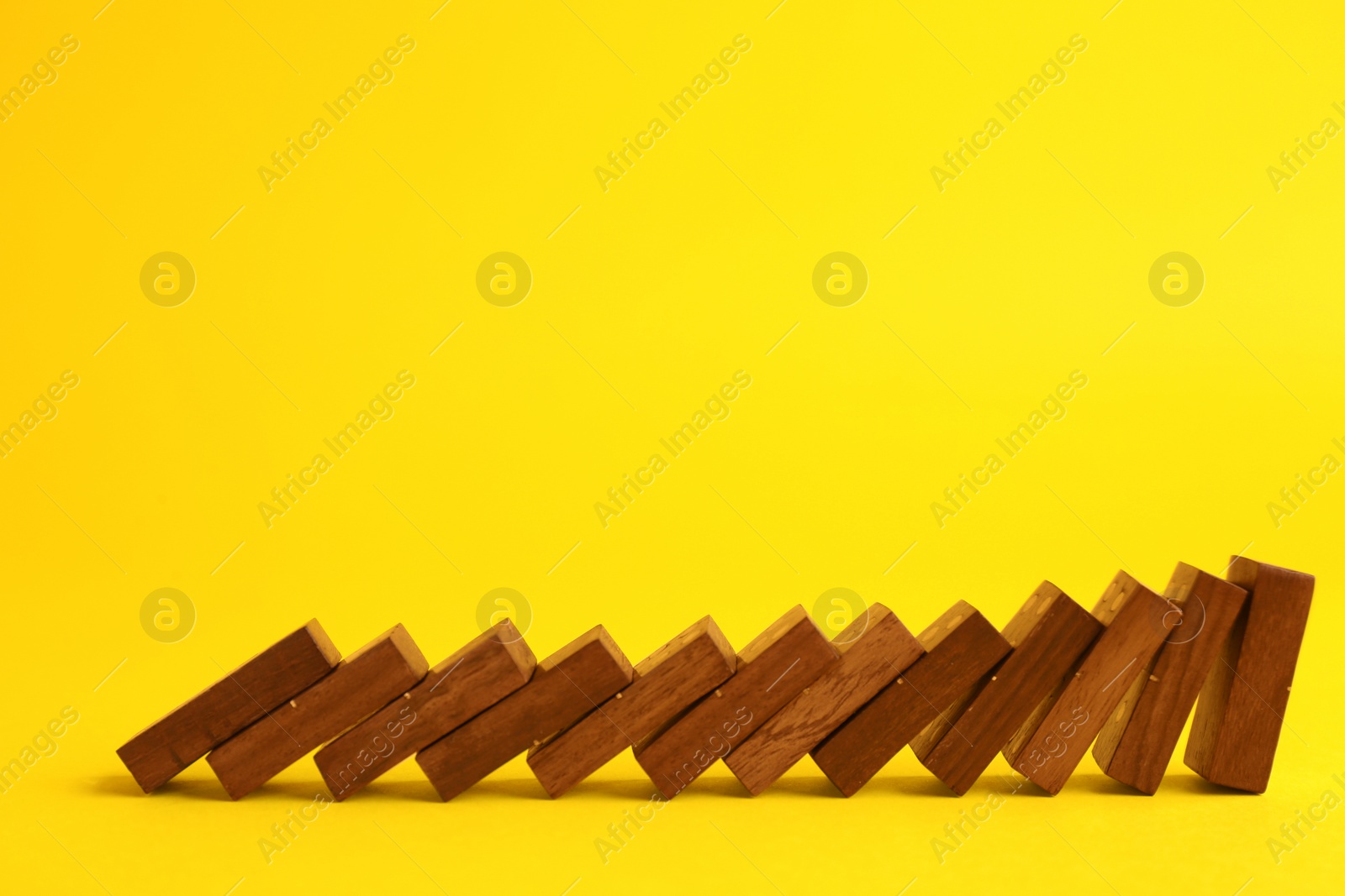 Photo of Falling wooden domino tiles on yellow background. Space for text