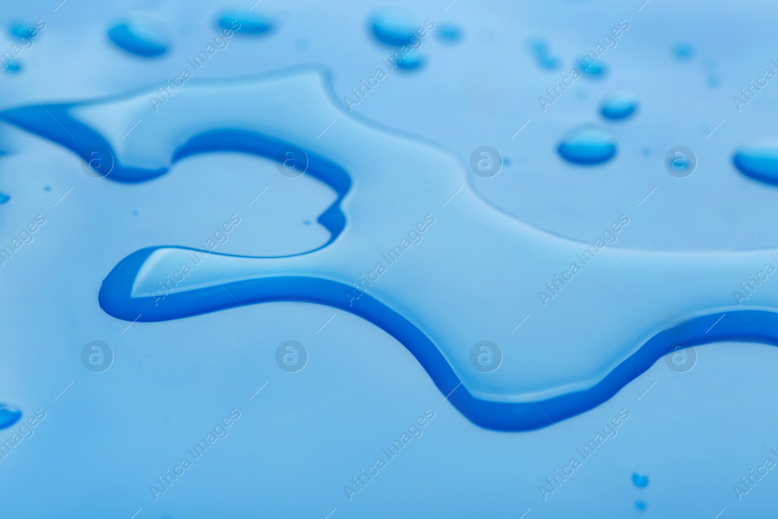 Photo of Drops of spilled water on blue background, closeup