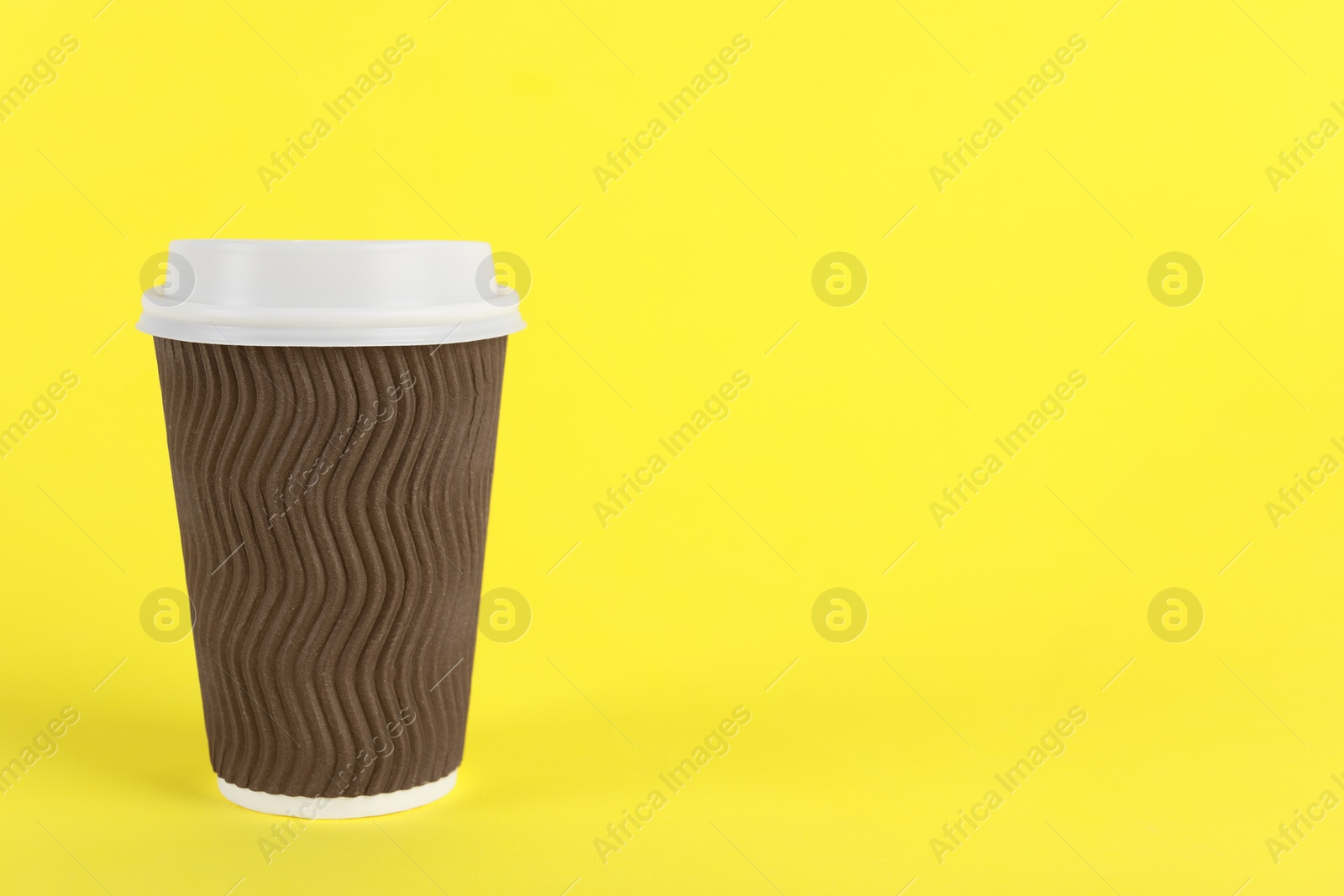 Photo of Brown paper cup with plastic lid on yellow background, space for text. Coffee to go