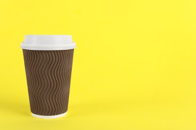 Photo of Brown paper cup with plastic lid on yellow background, space for text. Coffee to go