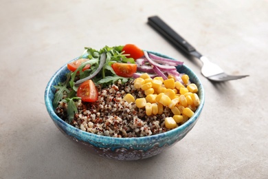 Photo of Healthy quinoa salad with vegetables in bowl and fork on table